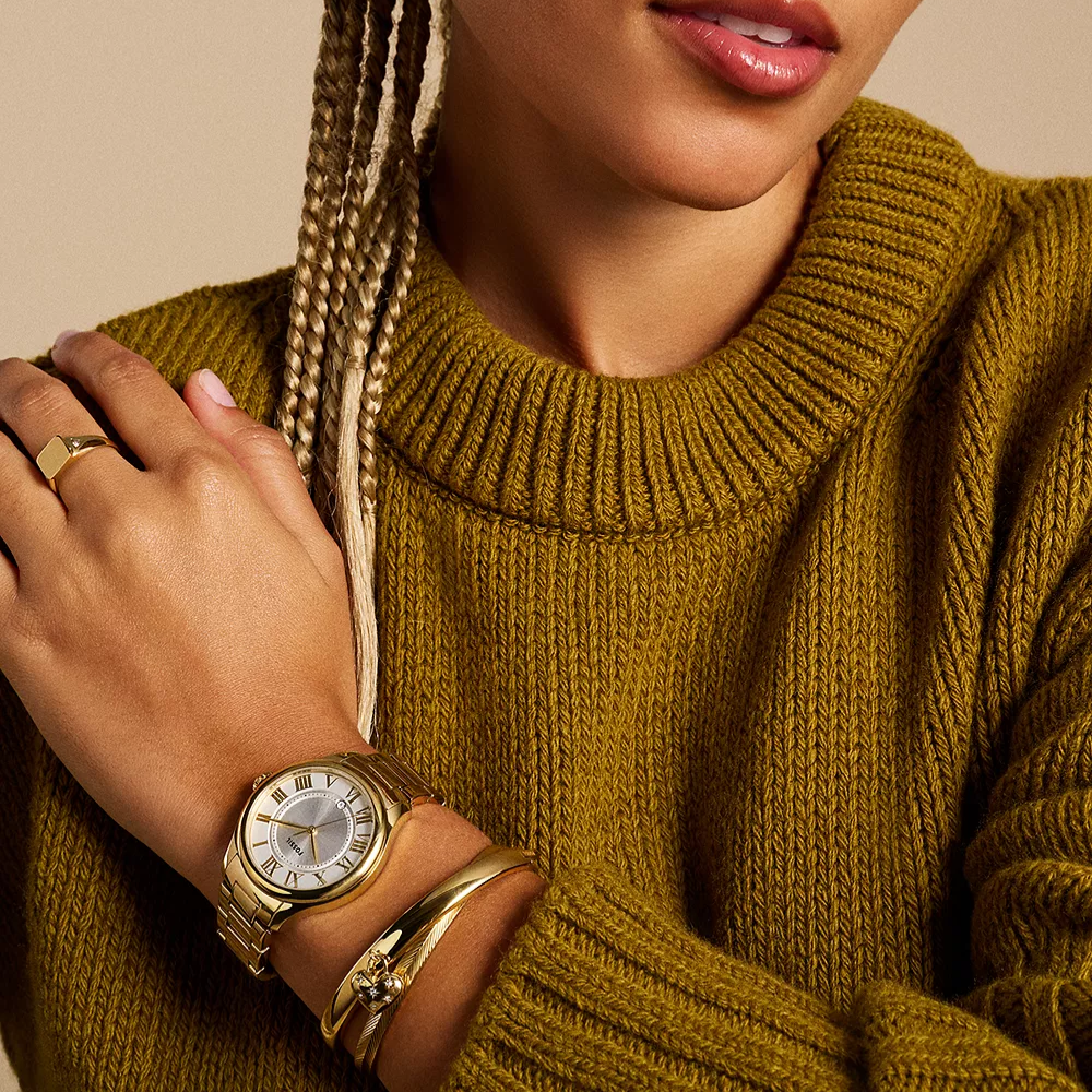 Person wearing a gold watch and bracelet on a mustard yellow sweater