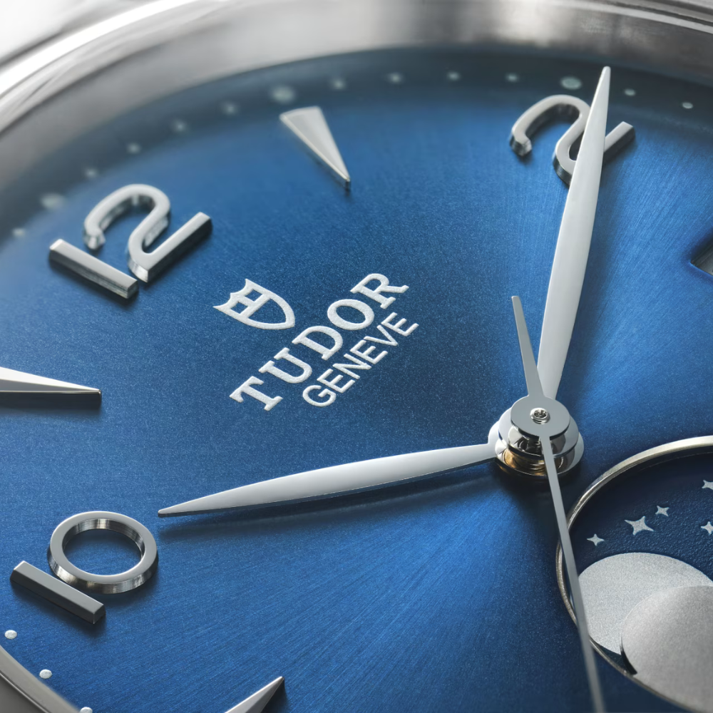 Close-up of a Tudor Luna watch face with blue background and silver accents. Text on watch readys "TUDOR Geneve"