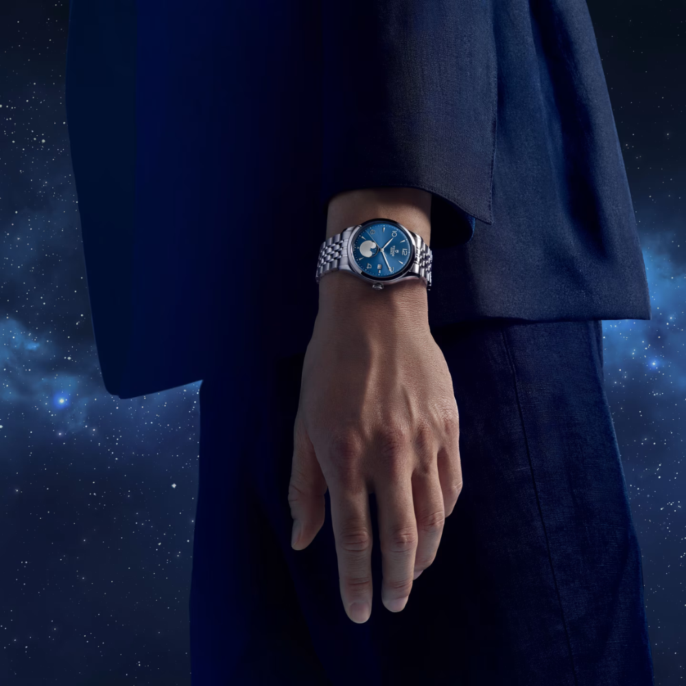 Hand wearing a steel, blue dial wristwatch with a starry night sky background